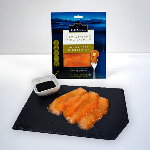 Salmón King ahumado Regal New Zealand en rebanadas sobre pizarra con empaque al fondo